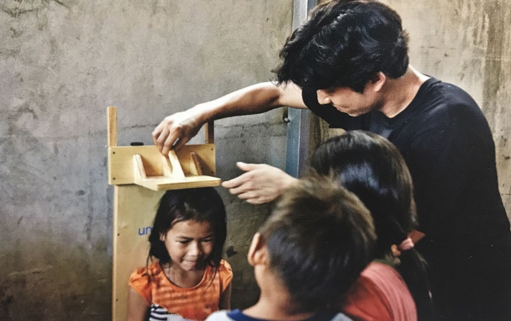 Founder Kim Seok-woo tenderly measuring the health and growth of a smiling little girl during field outreach