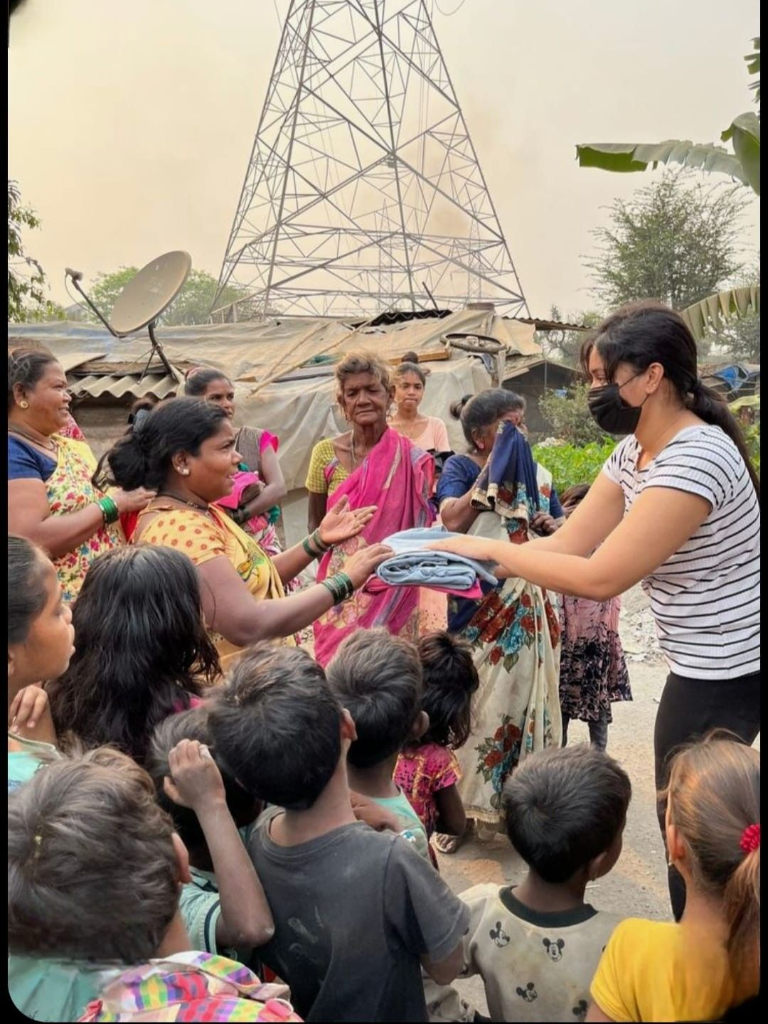 Foundation outreach volunteer handing warm clothing directly to an impoverished mother surrounded by community children